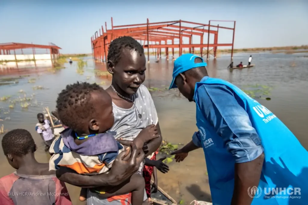 A UNHCR staff member helps Nyeritea Kay Nakney and her family out of their canoe and onto dry land at the IDP site in Bentiu.
