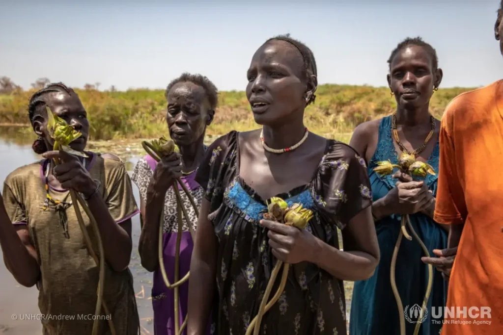 Nyepini Gator stands among a group of women who have just returned home with bundles of water lilies harvested from the floodwater.
